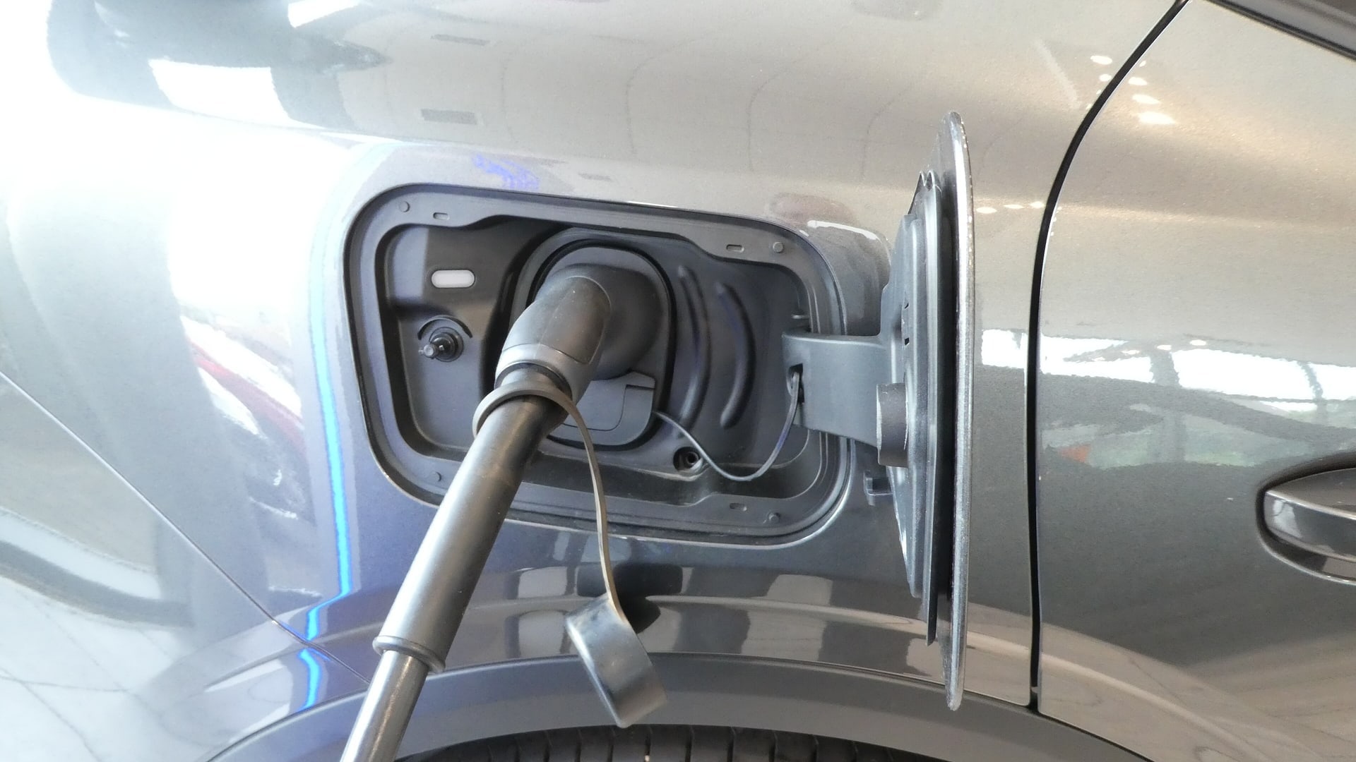 A charging cable plugged into the open charging port on the side of a grey electric car.